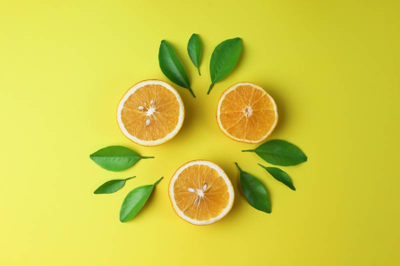 Frutas frescas de laranja com folhas verdes isoladas em fundo amarelo