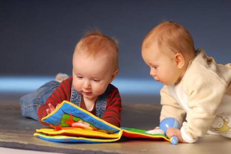 Foto de dois bebês brancos brincando com livro de brinquedo