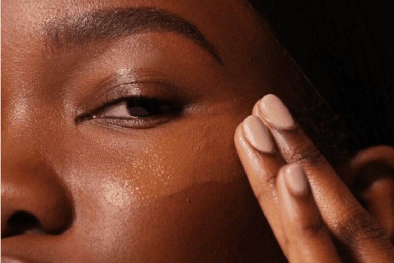 Mulher negra se maquiando, aplicando base no rosto