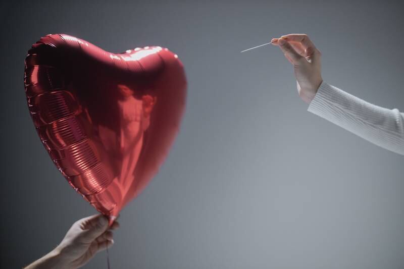 Balão em forma de coração prestes a ser estourado por agulha