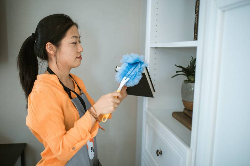 Mulher limpando objetos de uma casa com um espanador
