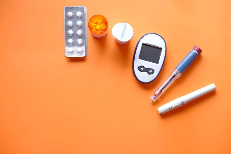 caneta de insulina, ferramentas de medição diabética e pílulas em fundo laranja