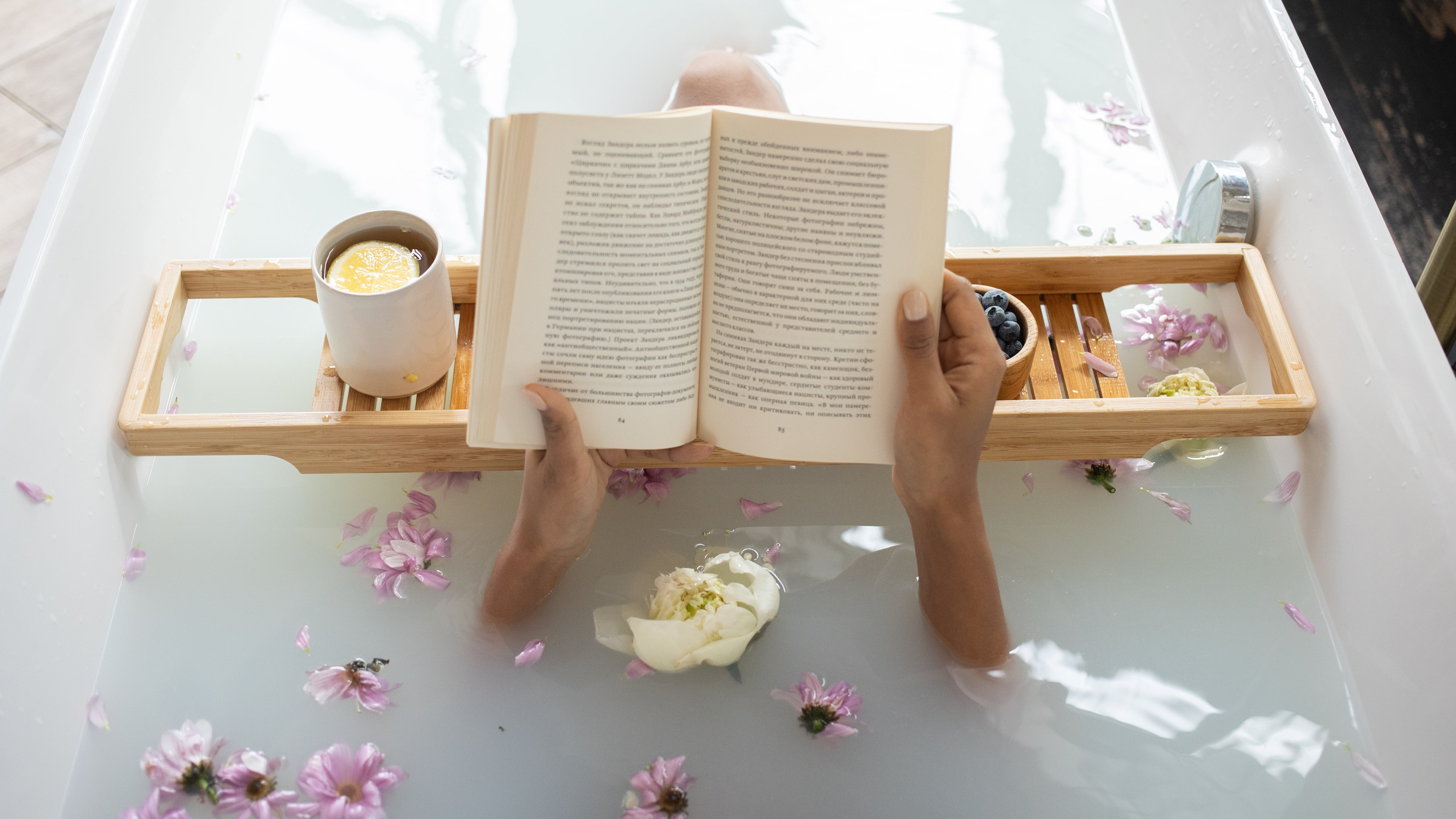 Mulher numa banheira com um livro e comida, referência a um spa caseiro