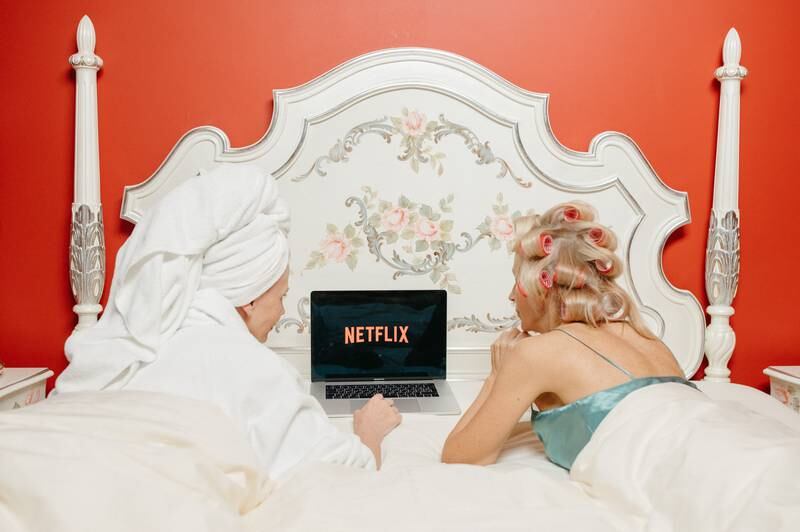 Duas amigas deitadas na cama vendo Netflix no computador