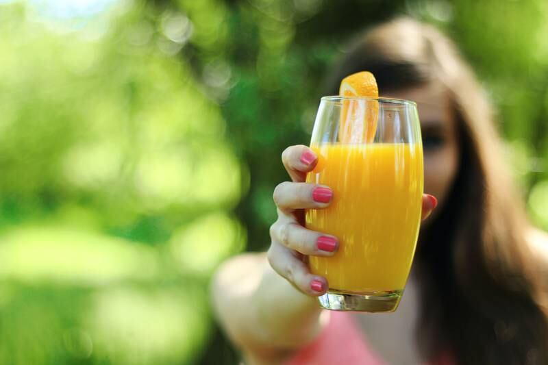 Mulher segurando copo de suco de laranja
