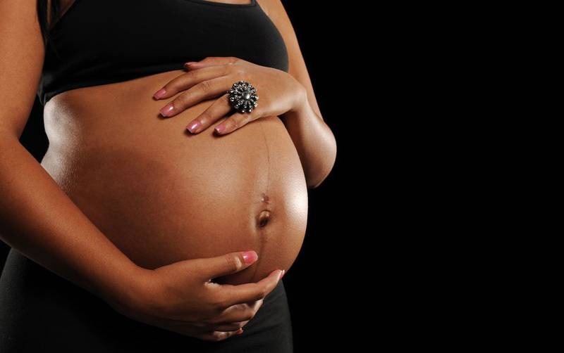 Mulher negra gravida com as mãos na barriga